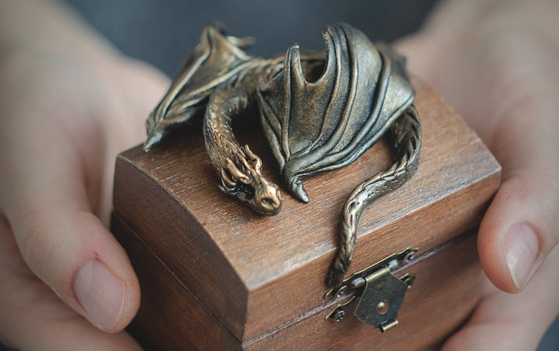 Hands holding a gift box with a decorative dragon on top.